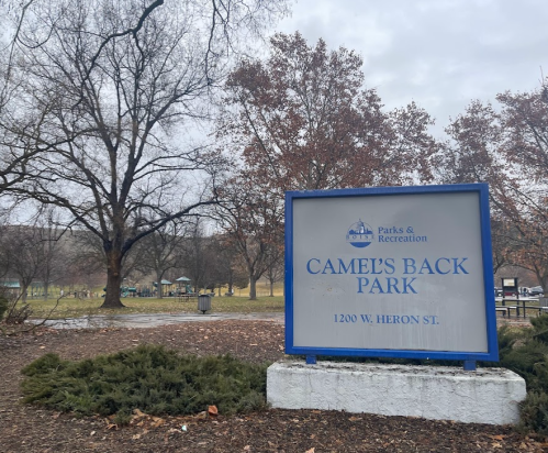 Sign for Camel's Back Park, featuring trees and a grassy area in the background, on a cloudy day.